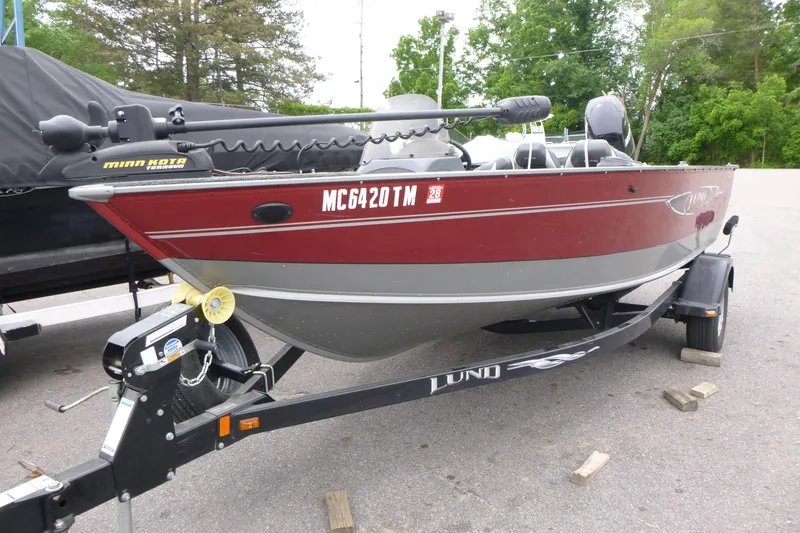 Slide: The Image of 2012 Lund 1775 Impact fishing boat on trailer, red and gray, parked outdoors. - 2