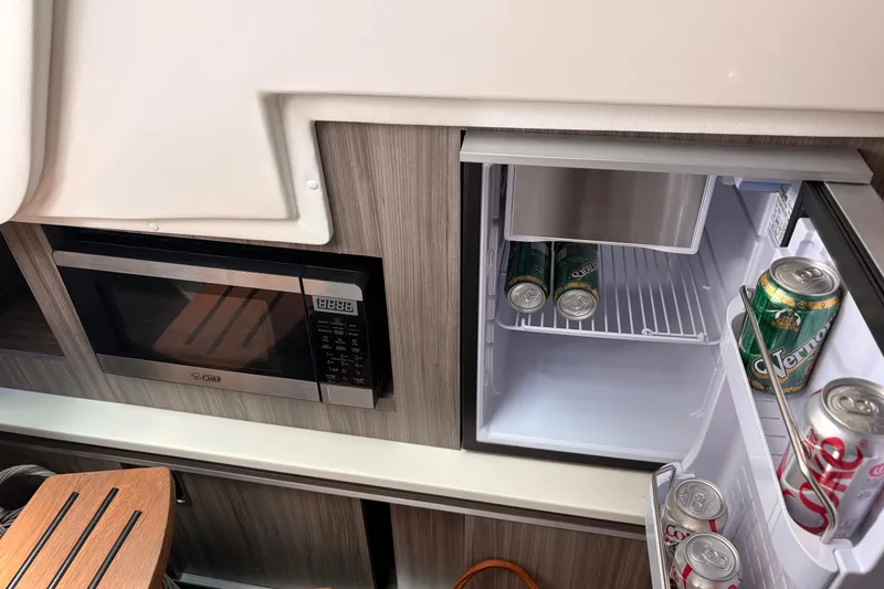 Slide: The Image of Compact kitchen area in 2026 Sea Ray Sundancer 320 with microwave and stocked mini fridge. - 18