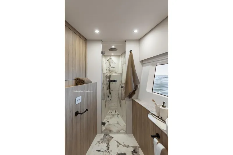 Slide: The Image of Luxurious yacht bathroom with modern shower, wooden accents, and ocean view window in Moon 60, 2025 model. - 16