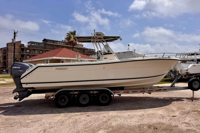 The Image of 2004 Pursuit 2670 Cuddy Console boat on trailer, parked outdoors under a cloudy sky. - 0