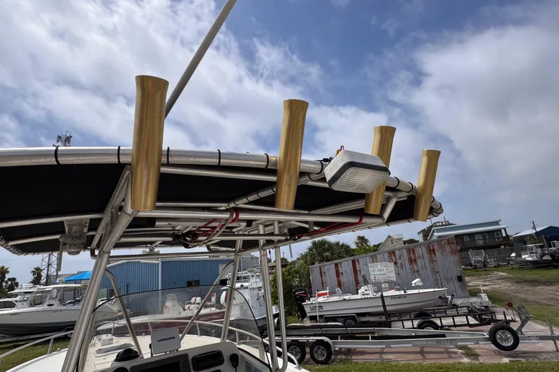 Slide: The Image of 2004 Pursuit 2670 Cuddy Console boat with rod holders and canopy, docked under a cloudy sky. - 54