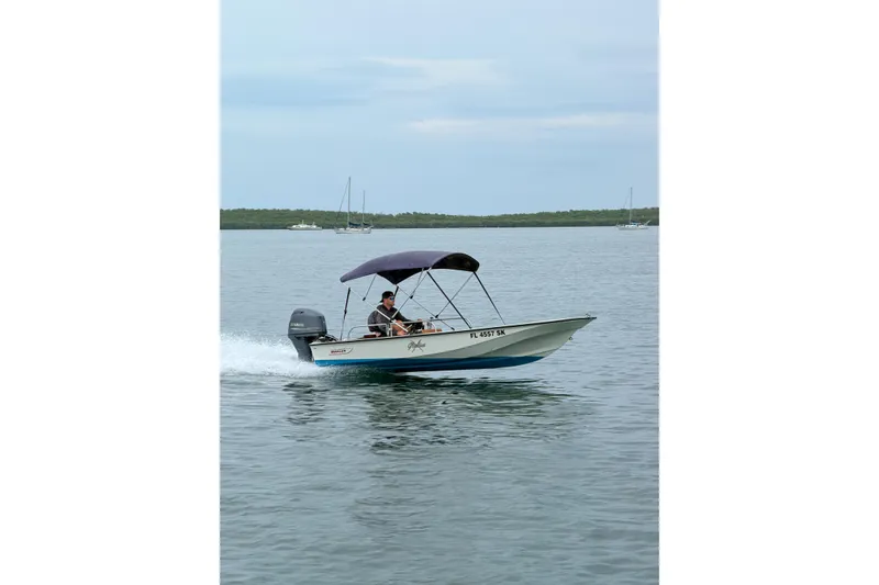 Slide: The Image of 1983 Boston Whaler 15 boat cruising on calm water with canopy and outboard motor. - 5