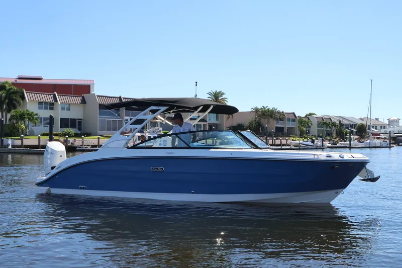 Slide: The Image of A blue 2027 Sea Ray SDX 270 Outboard boat on calm water, with modern buildings in the background. - 2