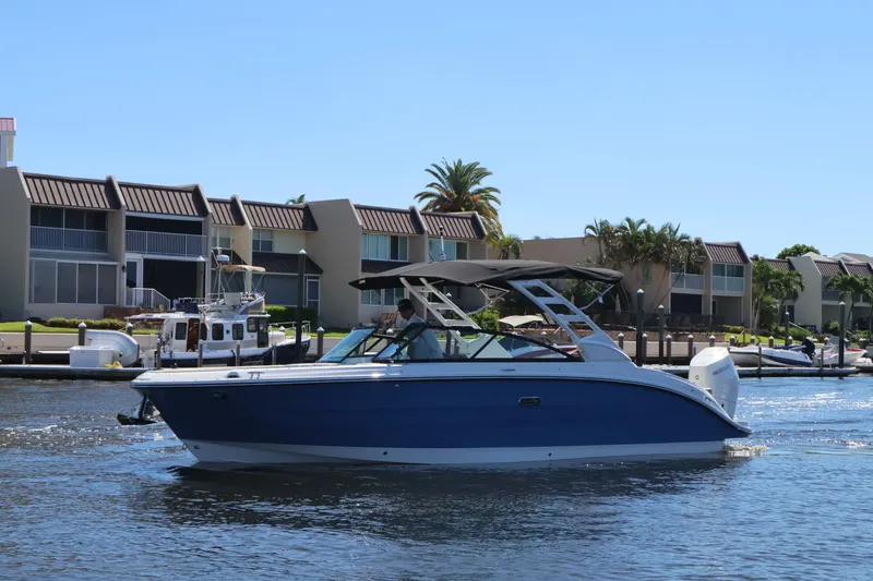 Slide: The Image of A 2027 Sea Ray SDX 270 Outboard cruising on a calm waterway in front of modern buildings. - 10