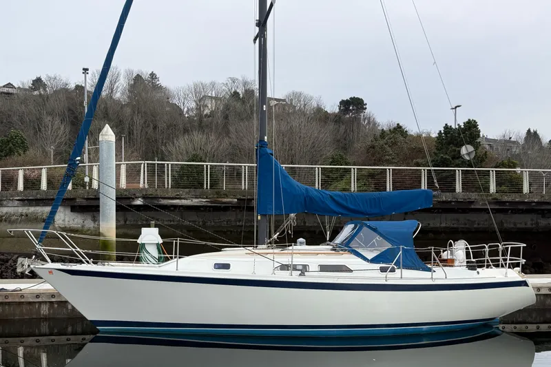 The Image of 1988 Ericson 32-200 sailboat docked, featuring blue sail cover and sleek white hull. - 0