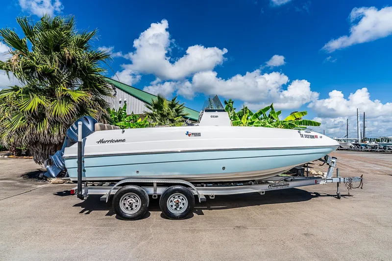 Slide: The Image of A 2016 Hurricane 21CC boat on a trailer, surrounded by palm trees and blue sky. - 2