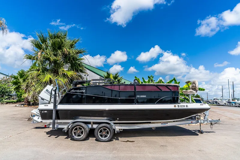 Slide: The Image of A 2022 Hurricane FD2260F boat on a trailer, surrounded by palm trees and blue sky. - 2