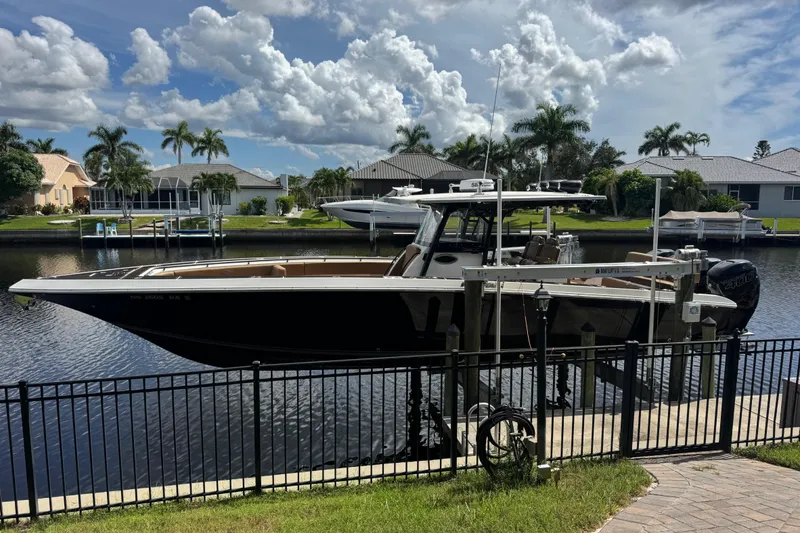 Slide: The Image of 2020 Fountain 38 Center Console boat docked by waterfront homes under a cloudy sky. - 7