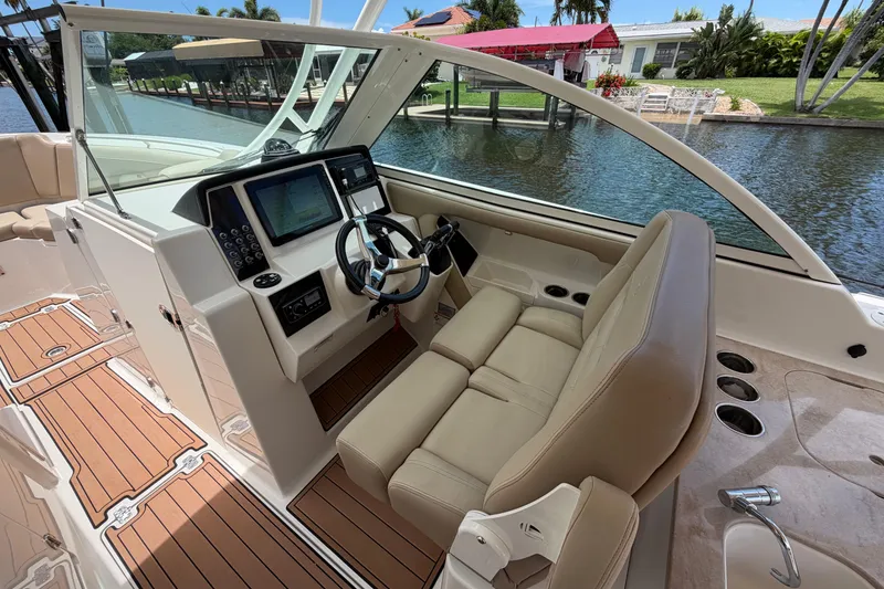 Slide: The Image of 2018 Sailfish 325 DC boat interior with helm, steering wheel, and navigation system by a canal. - 16