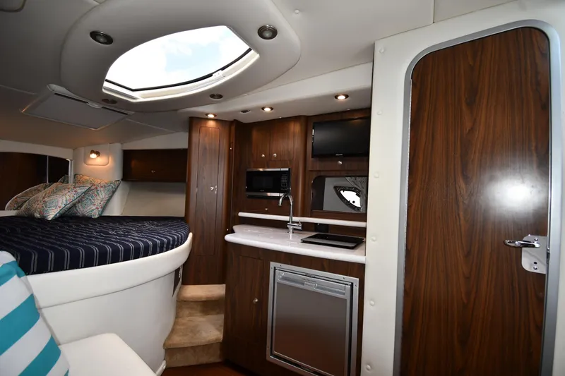 Slide: The Image of 2017 Rinker EX 320 cabin interior with bed, kitchenette, and wood accents. - 26