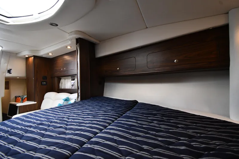 Slide: The Image of 2017 Rinker EX 320 cabin interior with striped bedding and wooden storage cabinets. - 28