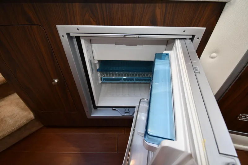 Slide: The Image of Open refrigerator in 2017 Rinker EX 320 boat interior, featuring wood paneling. - 33