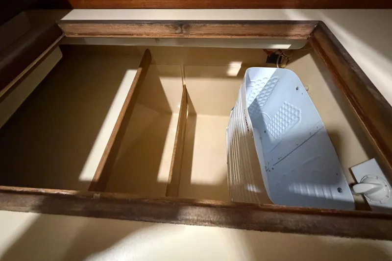 Slide: The Image of Storage compartment inside a 1990 Island Packet 38 sailboat, featuring wooden shelves and a white container. - 21
