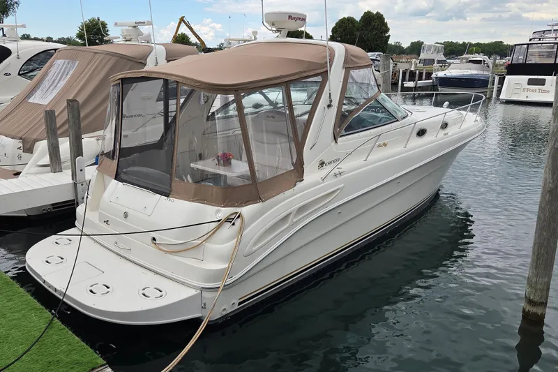 The Image of 1999 Sea Ray 340 Sundancer docked at marina, featuring tan canopy and sleek design. - 0