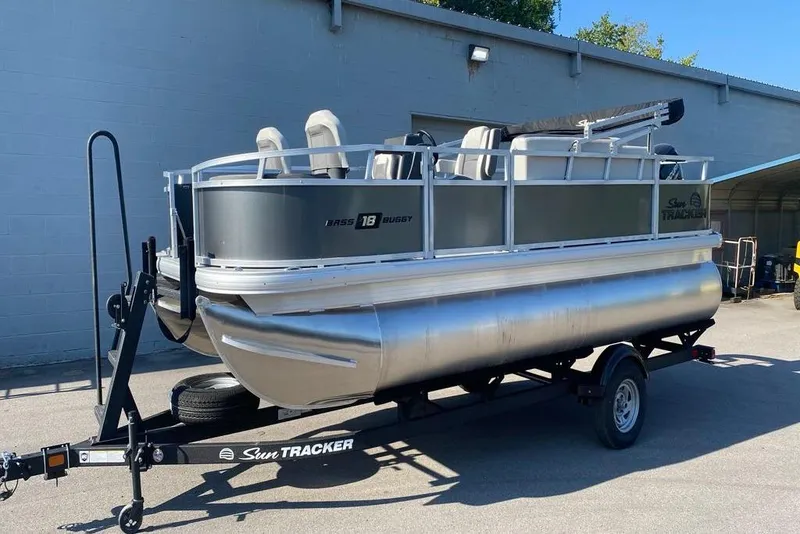 Slide: The Image of 2026 Sun Tracker Bass Buggy 18 DLX pontoon boat on trailer, parked outdoors. - 2