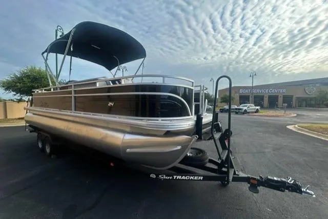 Slide: The Image of 2026 Sun Tracker Sportfish 24 XP3 pontoon boat on trailer, parked near boat service center. - 2