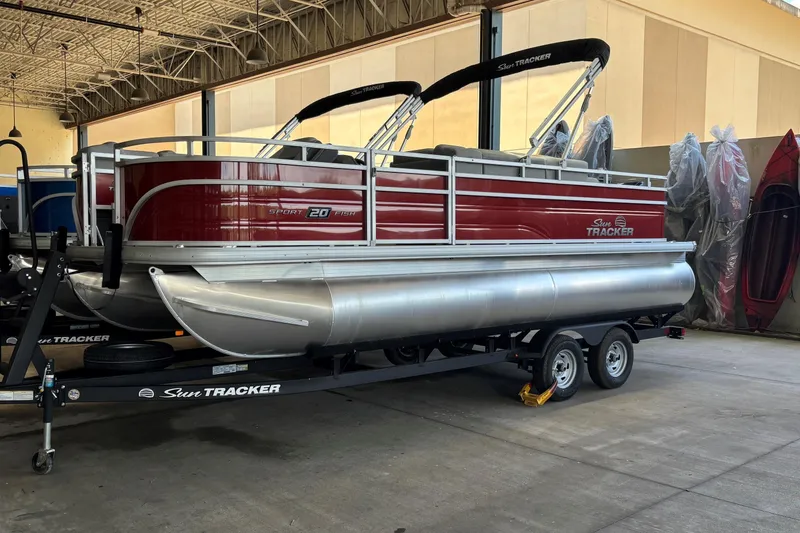 The Image of 2026 Sun Tracker SportFish 20 DLX pontoon boat on trailer in showroom. - 0