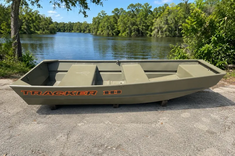The Image of 2026 Tracker Grizzly 10 Jon boat by a serene lake with lush greenery. - 0
