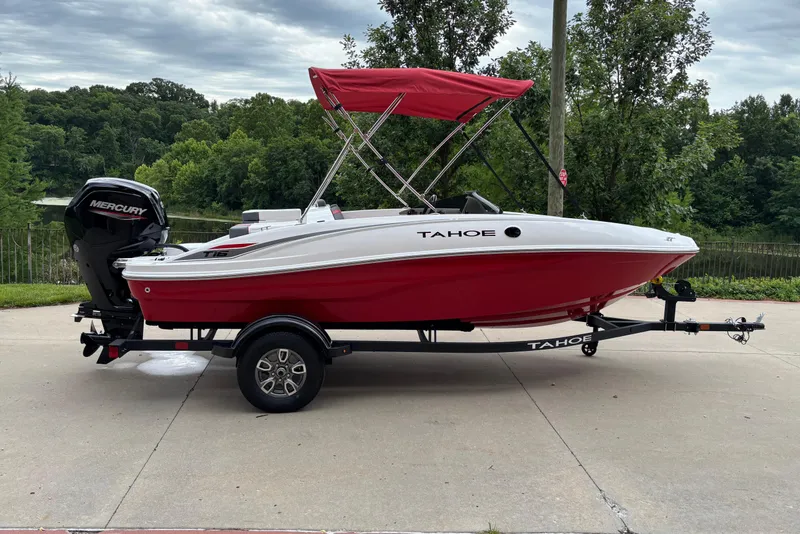 The Image of 2026 Tahoe T16 boat with red canopy on trailer, parked near lush greenery. - 0