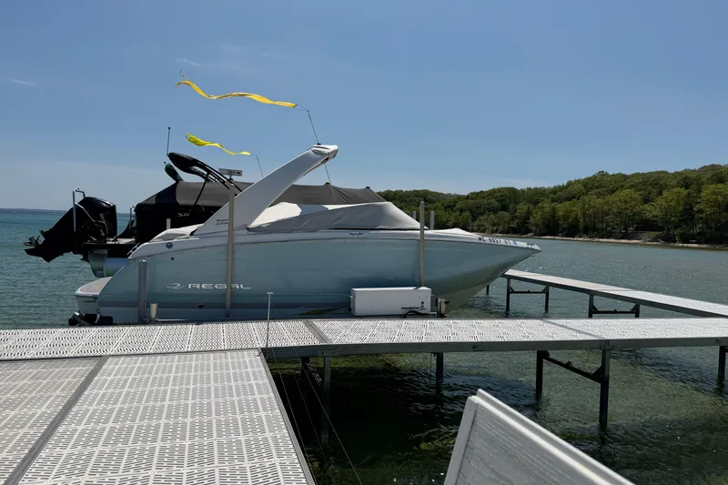Slide: The Image of 2022 Regal 22 FasDeck boat docked on a sunny lake with lush green shoreline. - 1
