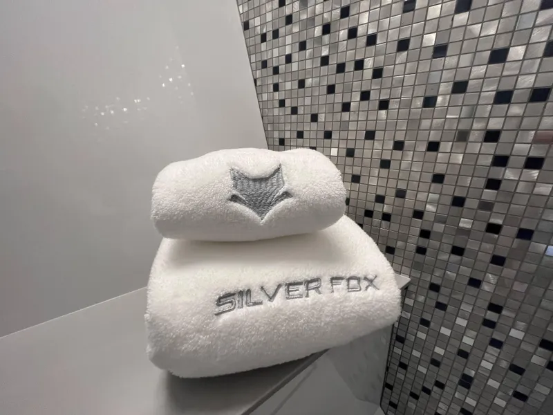 Slide: The Image of Stacked white towels with 'Silver Fox' embroidery in front of a mosaic wall. - 35