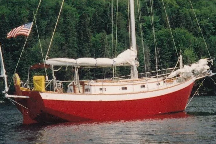 The Image of Red 1991 Hylan Offshore Steel Cutter sailboat on a calm lake with forest backdrop. - 0