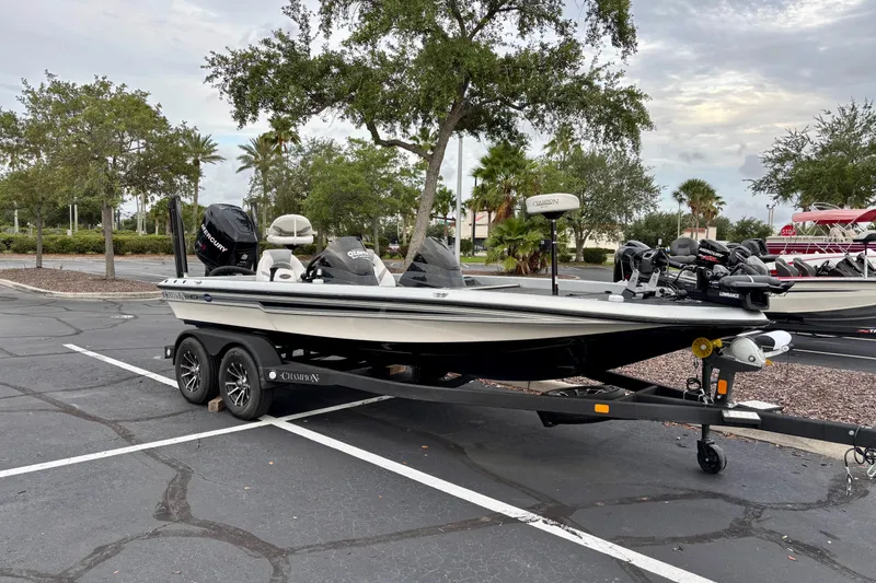 Slide: The Image of 2006 Champion 198 Elite boat parked in a lot, surrounded by trees and a cloudy sky. - 0