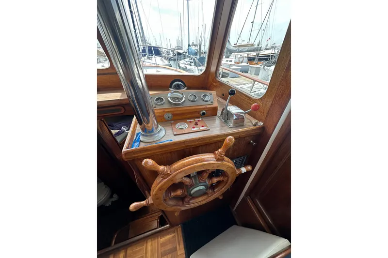 Slide: The Image of 1973 CHB 33 boat helm with wooden steering wheel and control panel in marina setting. - 15