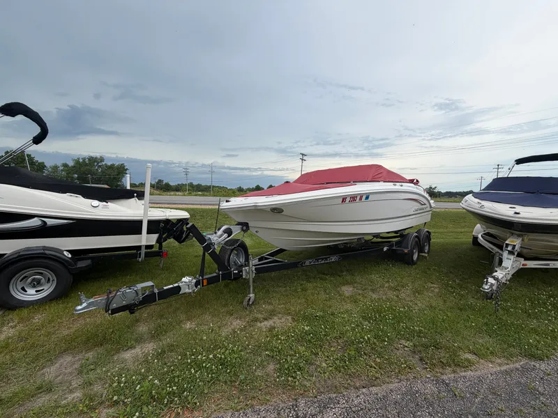 The Image of A 2012 Chaparral 206 SSi boat on a trailer, with a red cover, sits on grass. - 0