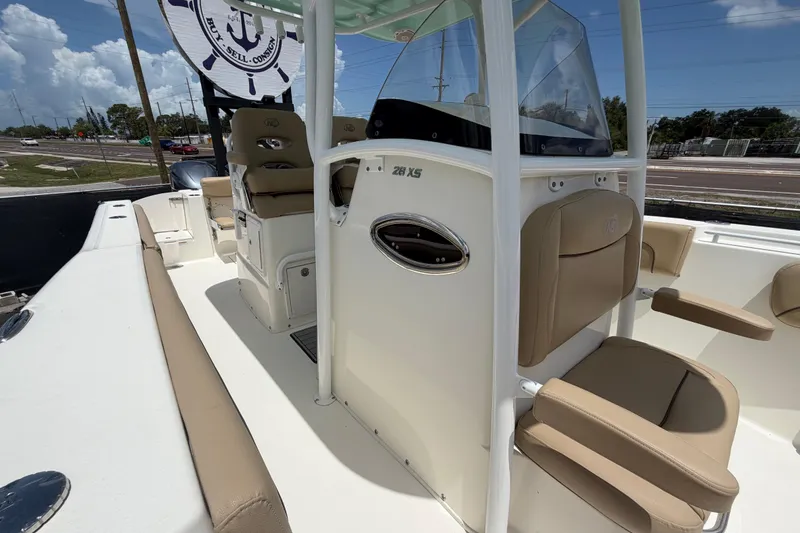 Slide: The Image of 2018 NauticStar 28 XS boat interior with beige seating and console, parked outdoors. - 57