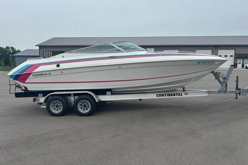 Slide: The Image of 1994 Formula 232 LS boat on trailer, featuring colorful stripes, parked near industrial buildings. - 1