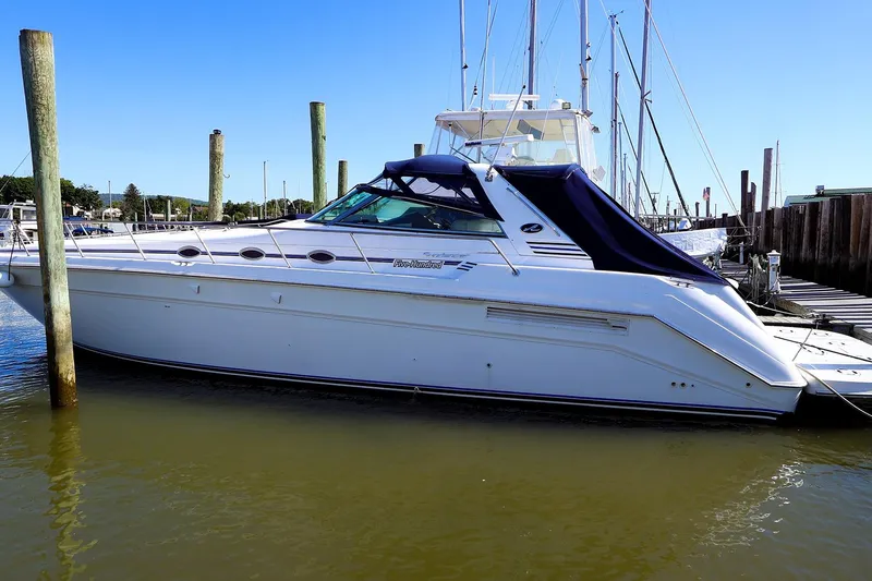 The Image of 1998 Sea Ray 500 Sundancer yacht docked at marina, featuring sleek white design and blue canopy. - 0