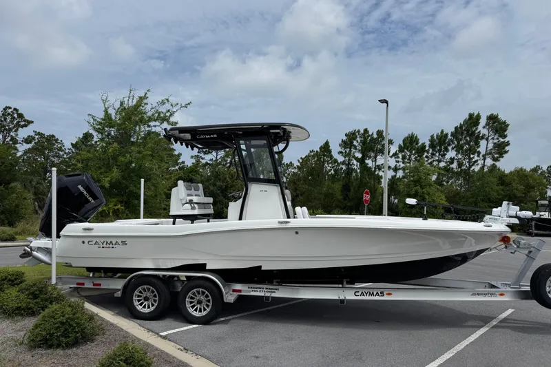 Slide: The Image of 2027 Caymas 26 HB boat on trailer in parking lot, surrounded by trees. - 2