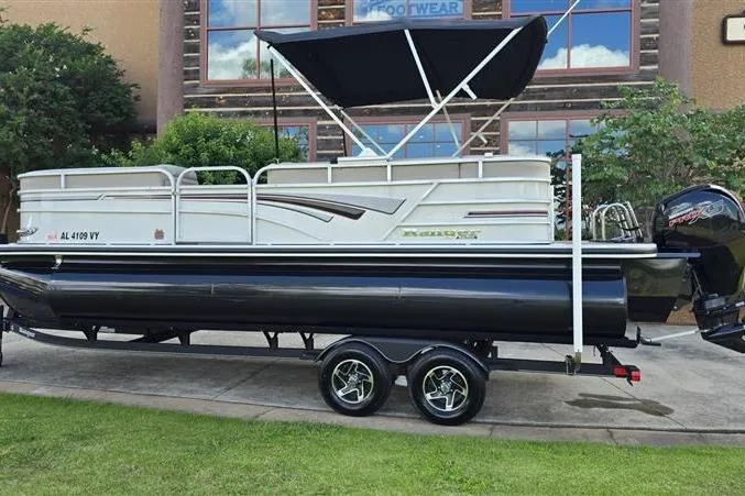Slide: The Image of 2023 Ranger Reata 223C pontoon boat with canopy on trailer, parked outdoors. - 2