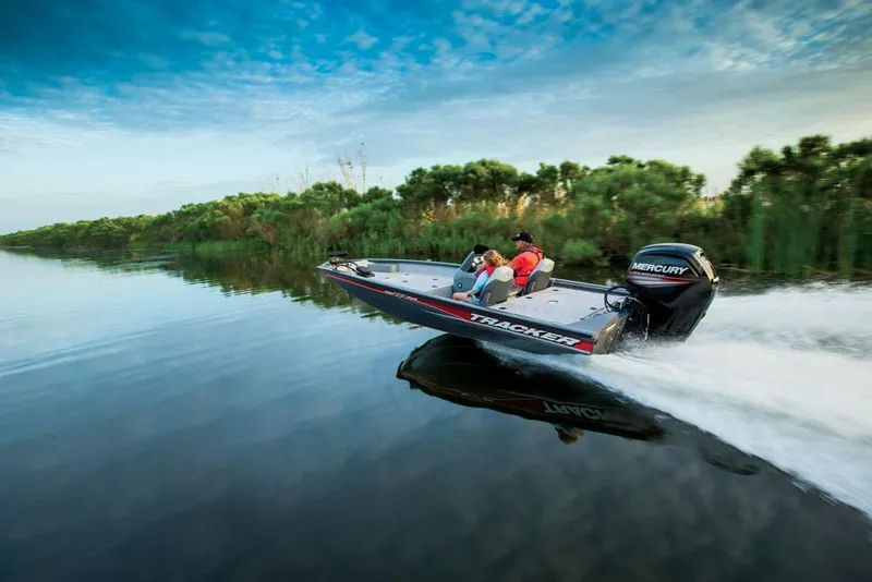 The Image of A Tracker boat speeds across calm water, surrounded by green vegetation. - 10