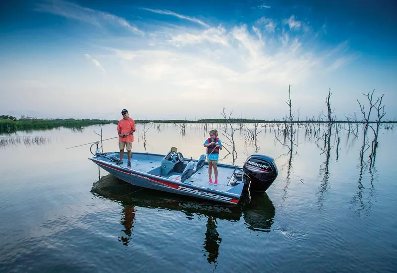 Slide: The Image of Two people fishing on a Tracker boat in a calm lake with bare trees. - 15