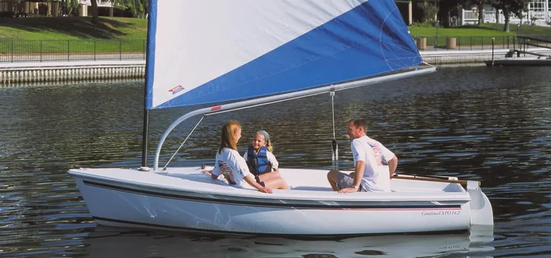 The Image of A white sailboat with a blue sail on calm water, occupied by three people. - 0