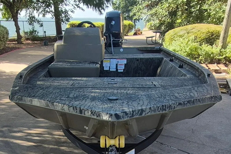 Slide: The Image of 2026 Tracker Grizzly 1648 SC boat with camouflage design, parked outdoors near a lake. - 2