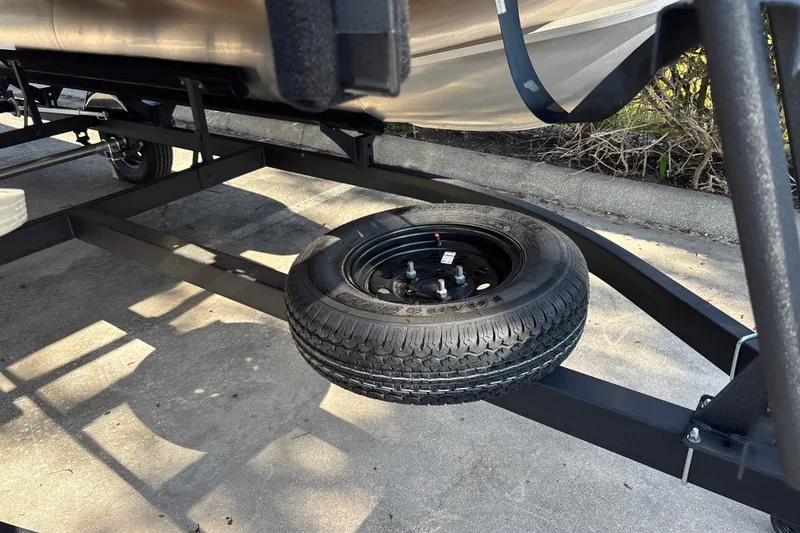 Slide: The Image of 2026 Sun Tracker Party Barge 16 DLX trailer with spare tire on concrete surface. - 26