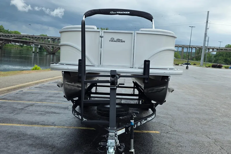 Slide: The Image of 2026 Sun Tracker Party Barge 20 DLX on trailer by a river. - 2