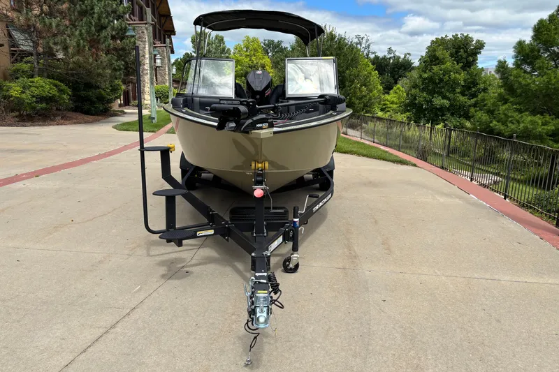 Slide: The Image of 2026 Tracker Targa V-18 Combo boat on trailer, parked on a driveway with lush greenery. - 2