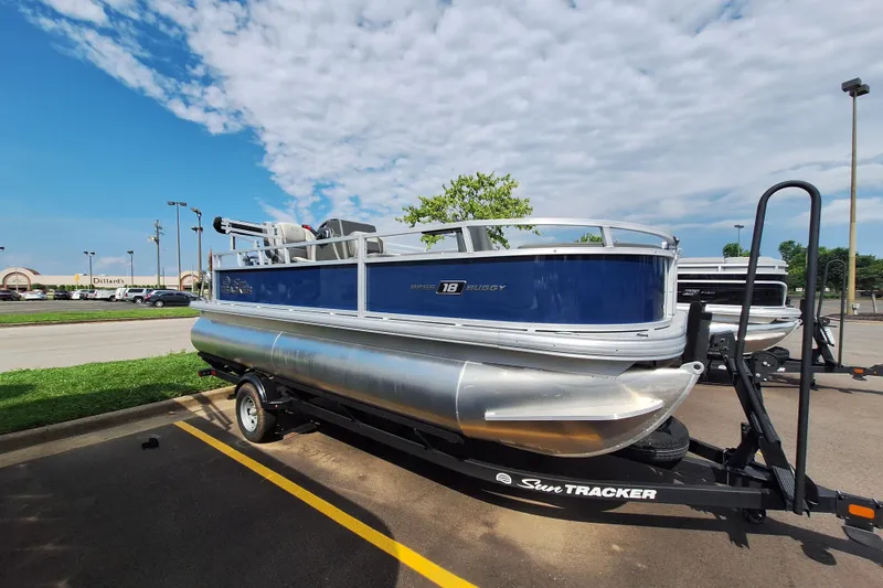 Slide: The Image of 2026 Sun Tracker Bass Buggy 18 DLX pontoon boat on trailer in parking lot. - 2