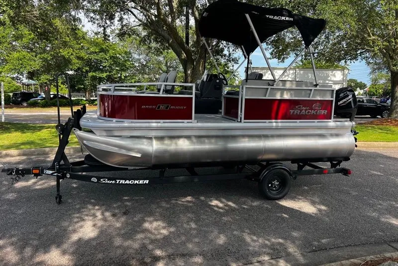 The Image of 2026 Sun Tracker Bass Buggy 16 XL Select pontoon boat on trailer, parked outdoors. - 0