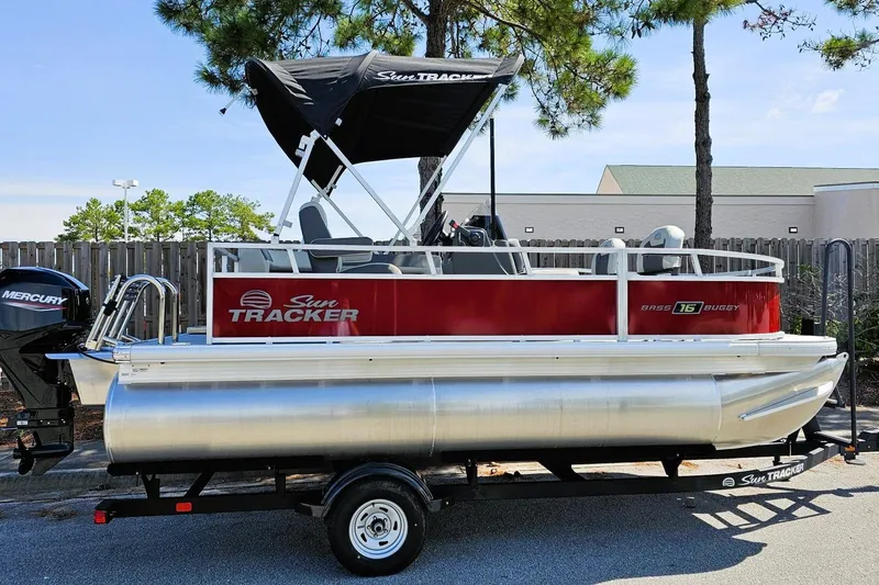 The Image of 2026 Sun Tracker Bass Buggy 16 XL Select pontoon boat on trailer, parked outdoors. - 0