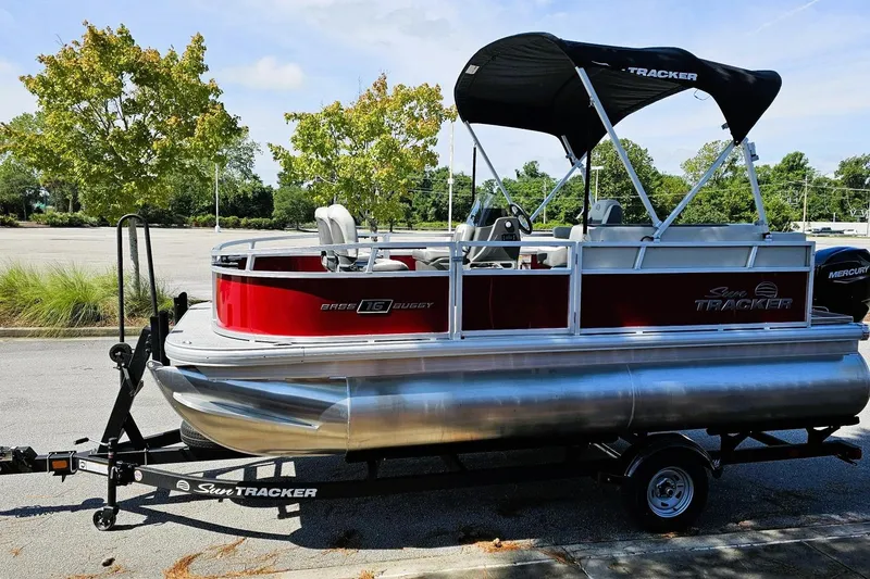 Slide: The Image of 2026 Sun Tracker Bass Buggy 16 XL Select pontoon boat on trailer, parked outdoors. - 3