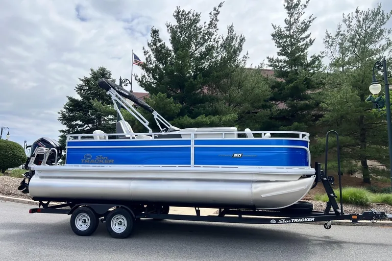 Slide: The Image of 2026 Sun Tracker Fishin' Barge 20 DLX pontoon boat on trailer, parked outdoors. - 1