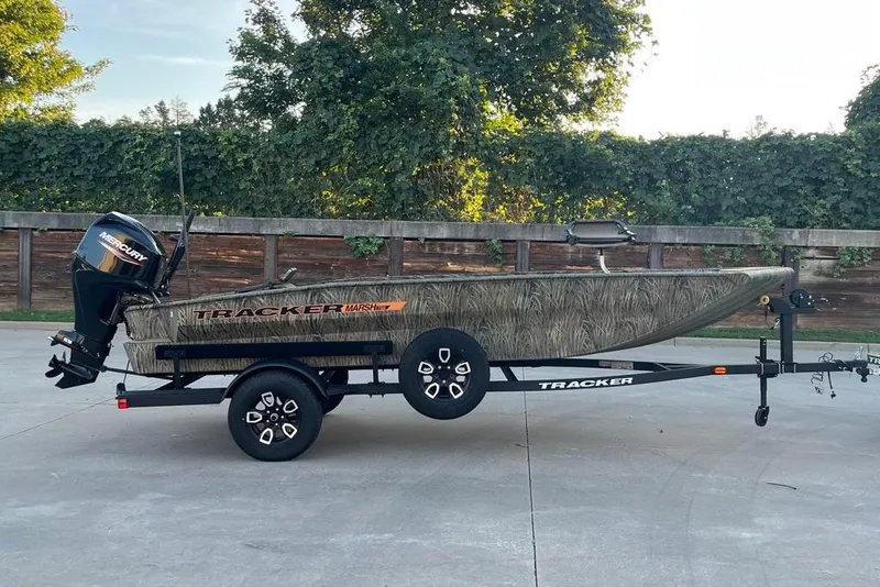 The Image of 2026 Tracker Grizzly 1756 T Marsh boat on trailer, camo design, parked outdoors. - 0
