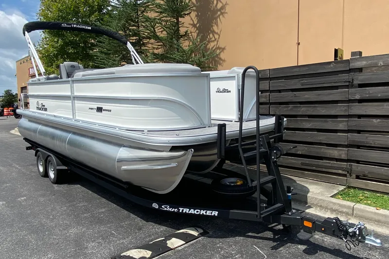 Slide: The Image of 2026 Sun Tracker Party Barge 22 XP3 pontoon boat on trailer, parked outdoors. - 2