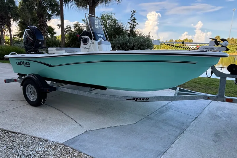 Slide: The Image of 2026 Mako Pro Skiff 15 CC boat on trailer, parked outdoors near water. - 1
