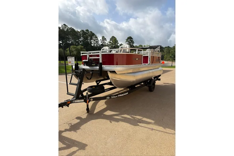 The Image of 2026 Sun Tracker Bass Buggy 16 XL Select pontoon boat on trailer, parked outdoors. - 0